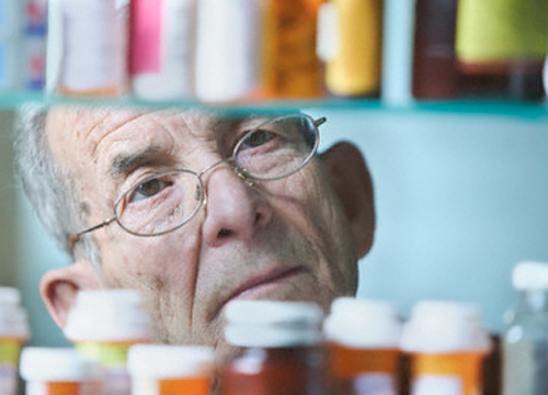 Imagen de un hombre de unos setenta años de edad trás unos botes de medicamentos